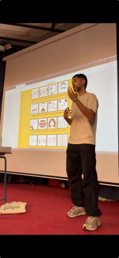 Persona de pie frente a una pantalla, presentando información con gestos.